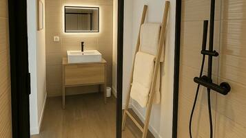 Un baño moderno con mampara de vidrio, suelo de madera, lavamanos y zona de ducha.