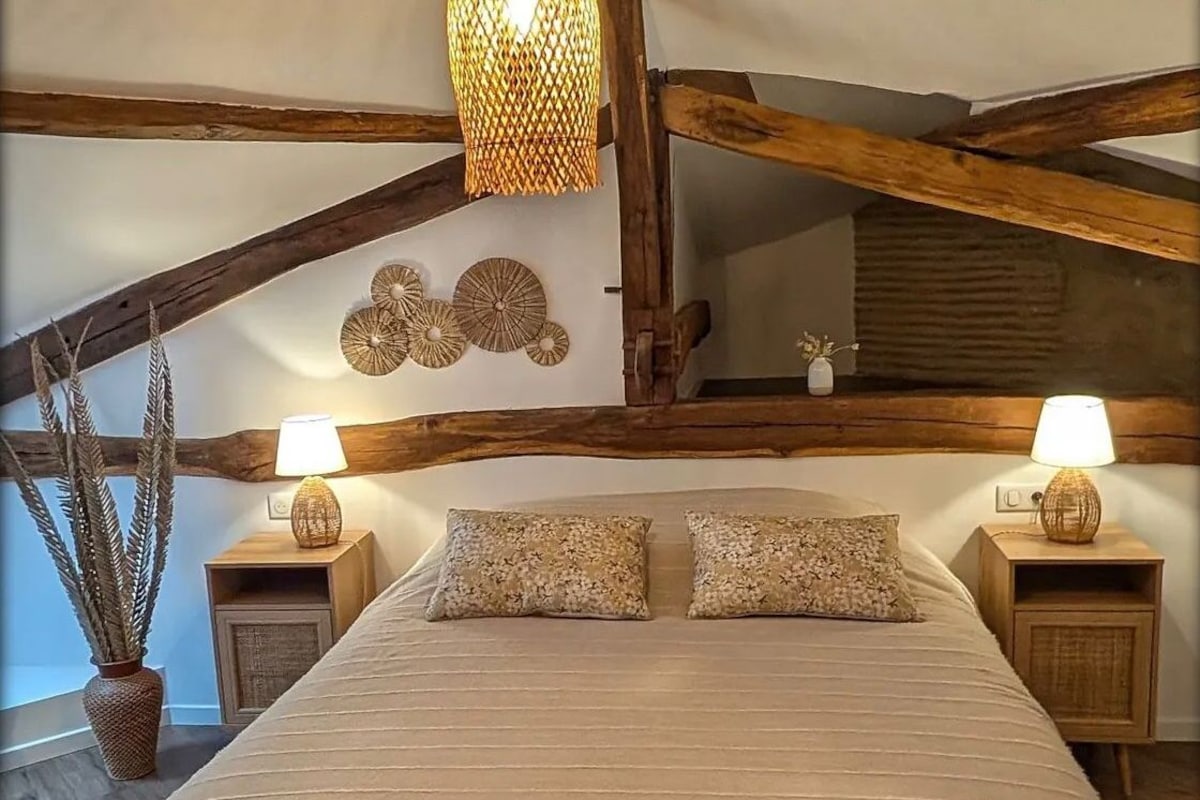 A bedroom with a large bed, wooden beams, a hanging light fixture, and two bedside tables with lamps.
