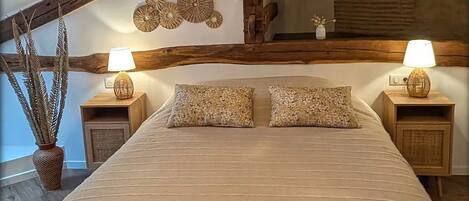 Un dormitorio con una cama grande, vigas de madera, una lámpara colgante y dos mesitas de noche con lámparas.