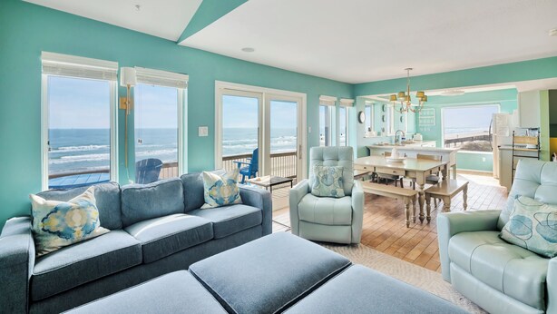 Una sala de estar con un ventanal grande con vista al océano, un comedor con mesa y sillas, y una zona de estar con sofá y sillones.