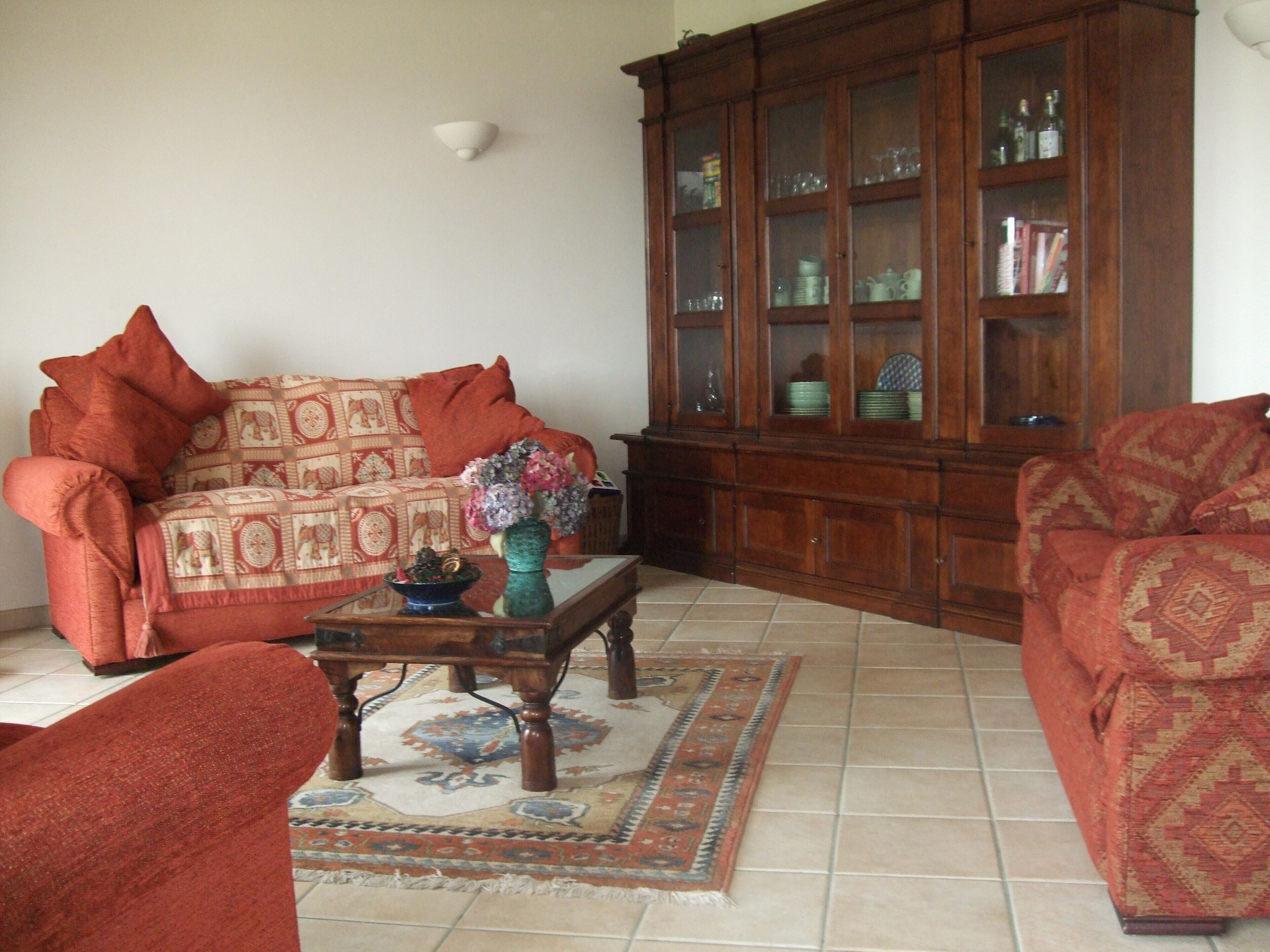 Una sala de estar con un sofá estampado, un mueble con puertas de vidrio y un jarrón decorativo sobre una mesa de centro.