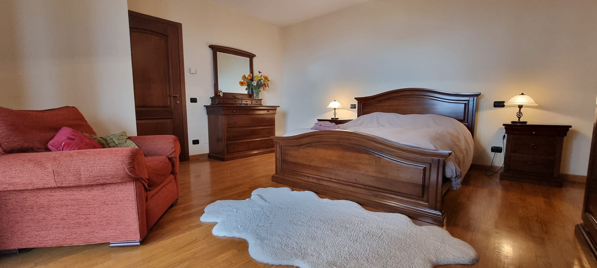 A bedroom with a wooden bed, a red sofa, a dresser, and a mirror.