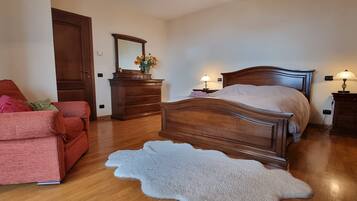 A bedroom with a wooden bed, a red sofa, a dresser, and a mirror.