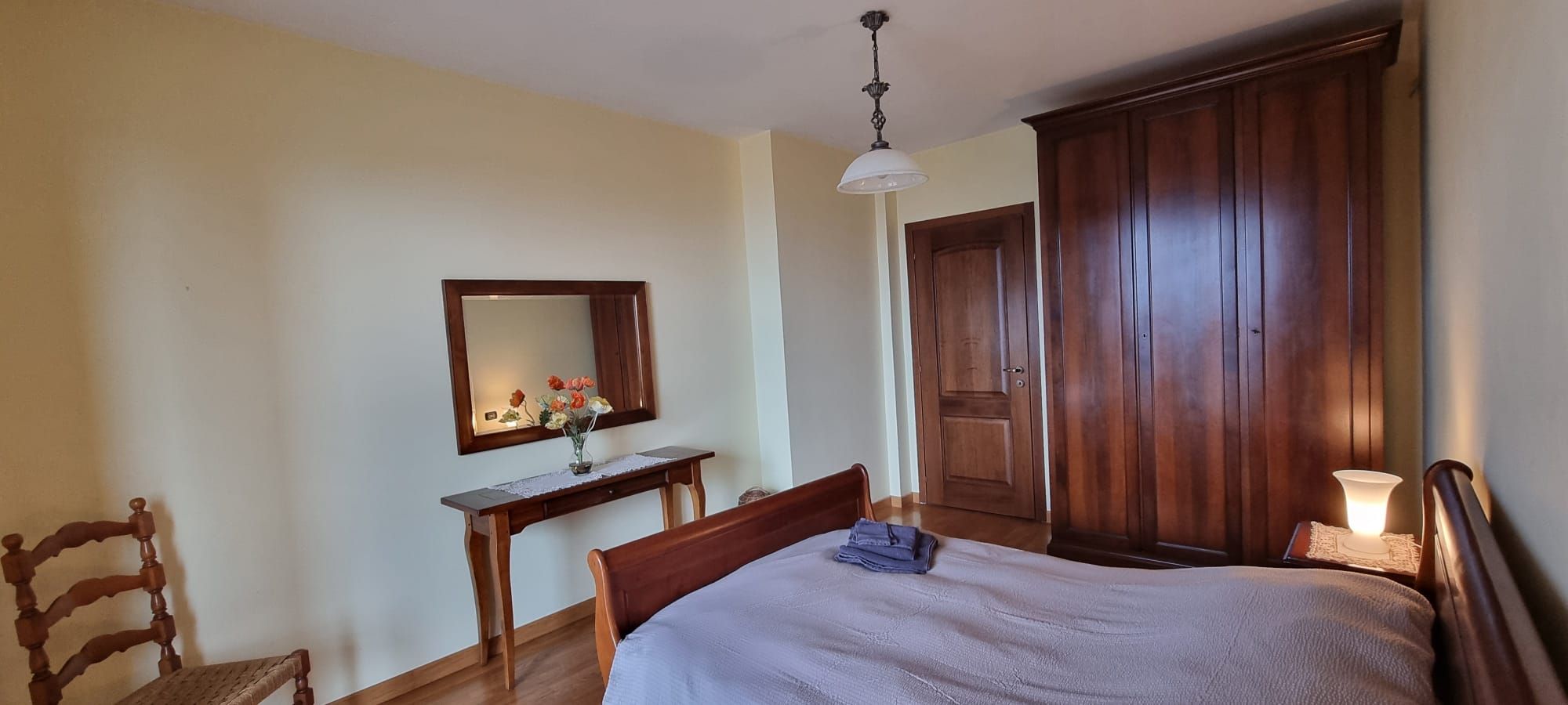 Une chambre à coucher avec un lit, un bureau en bois, une chaise, une armoire et un miroir au mur.