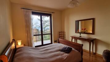 Ein Schlafzimmer mit einem Bett, einem Nachttisch, einem Spiegel und einem Fenster mit Vorhängen.