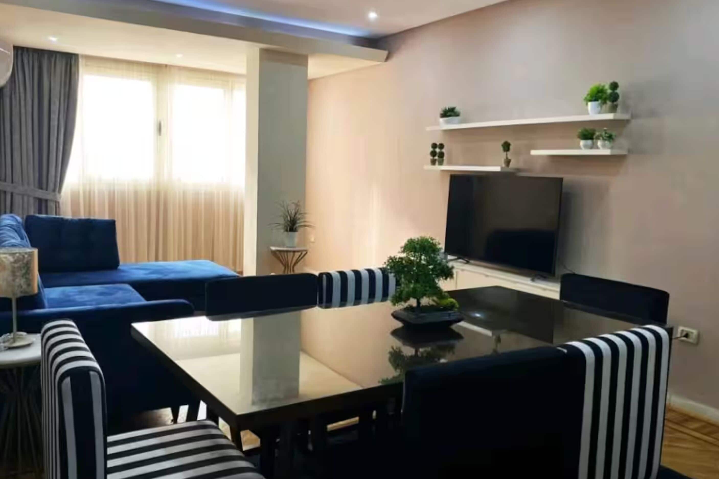 Una sala de estar moderna con un sofá, sillas a rayas, una mesa de vidrio y un televisor.