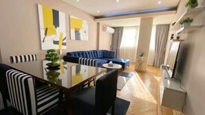 Una sala de estar moderna con un sofá azul, una mesa de comedor con sillas y un televisor montado en la pared.