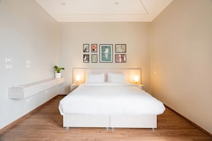Ein modernes Hotelzimmer mit einem großen Bett, Nachttischen mit Lampen, einer integrierten Ablage und einem Kunstwerk an der Wand.