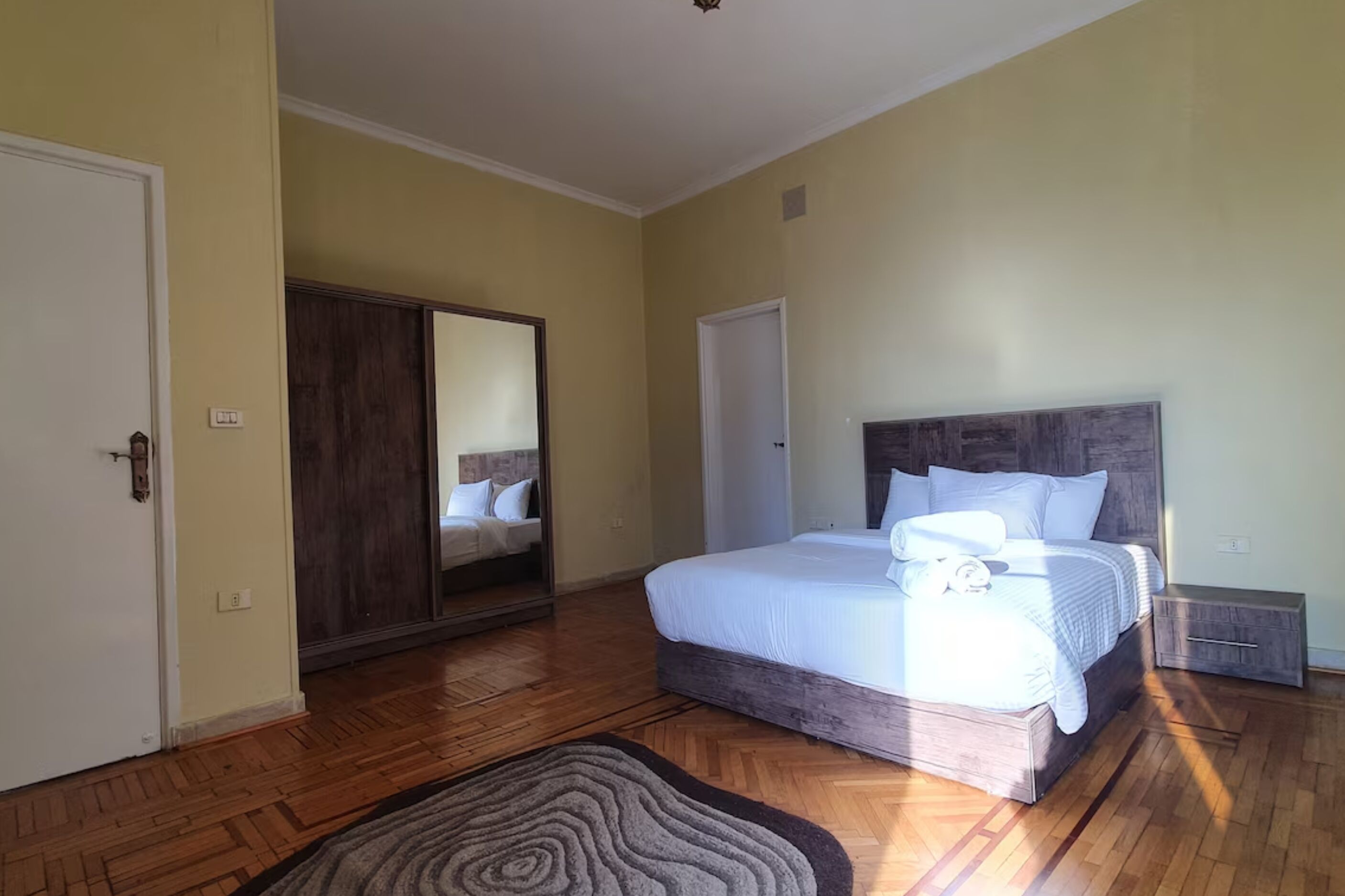 A bedroom with a large bed, a wardrobe, and a mirror.