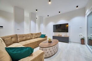 En moderne stue med en beige hjørnesofa, et rundt sofabord og et fladskærms-tv monteret på væggen.