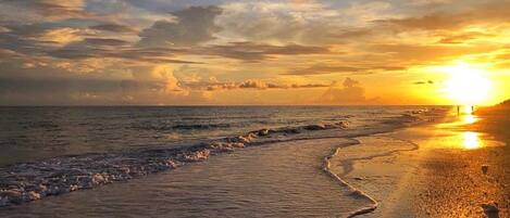 A beach scene with waves lapping onto the shore and a sunset in the background.