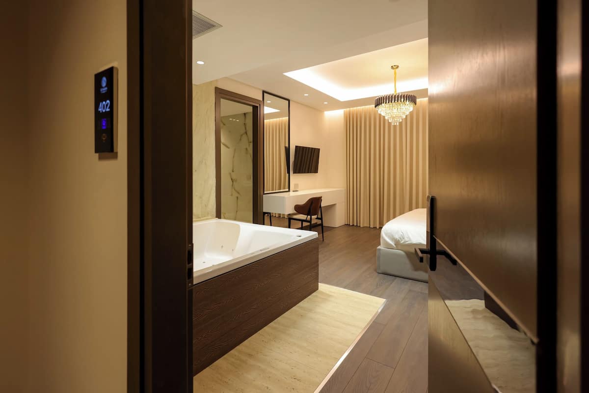 Una habitación de hotel moderna con una bañera grande, zona de ducha separada, tocador con espejo, cama y candelabro.