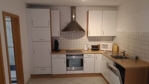 Een compacte keuken met witte kastjes, een roestvrijstalen afzuigkap, een magnetron en een vaatwasser.