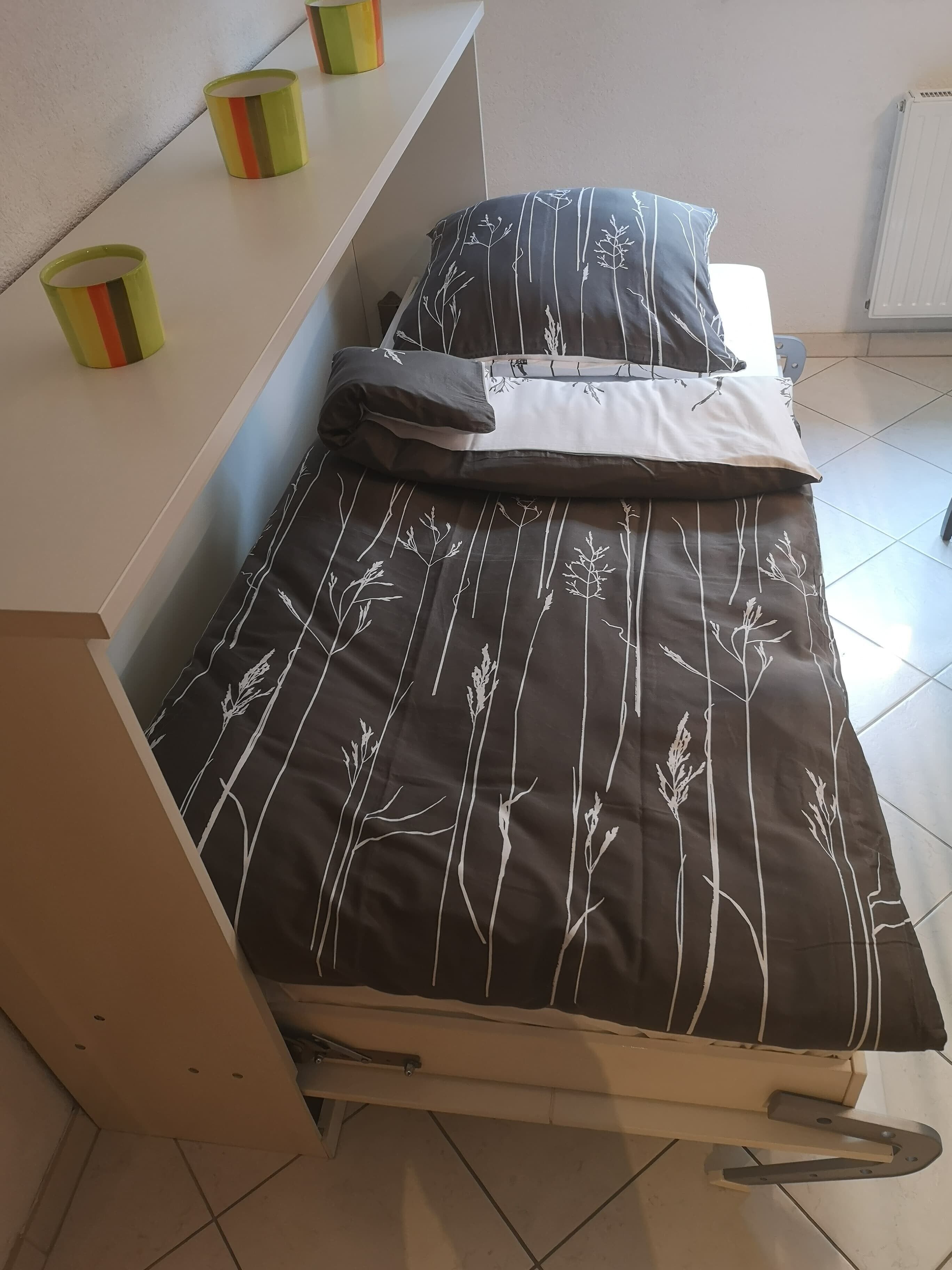 Een bed met een bruin-wit bloemenbed en een kussen, en een nachtkastje met een kop.