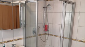Een badkamer met een douche met glazen wand, een wastafel en een spiegel.