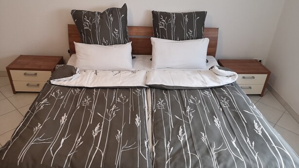 Een bed met een donker beddegoed met patroon, twee witte kussens en een houten hoofdbord.
