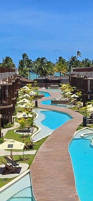 A resort with a winding pool, palm trees, and wooden walkways. - Naay Villas Boutique (Porto de Pedras)