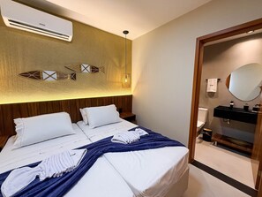 A hotel room with a bed, a bedside table, a wall-mounted air conditioner, a decorative wall piece, a hanging light fixture, a bathroom with a sink and mirror. - Naay Villas Boutique (Porto de Pedras)