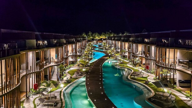 A modern hotel with a central swimming pool, multiple balconies, and outdoor seating areas.