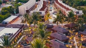 An aerial view of a resort with multiple buildings, palm trees, and a swimming pool.
