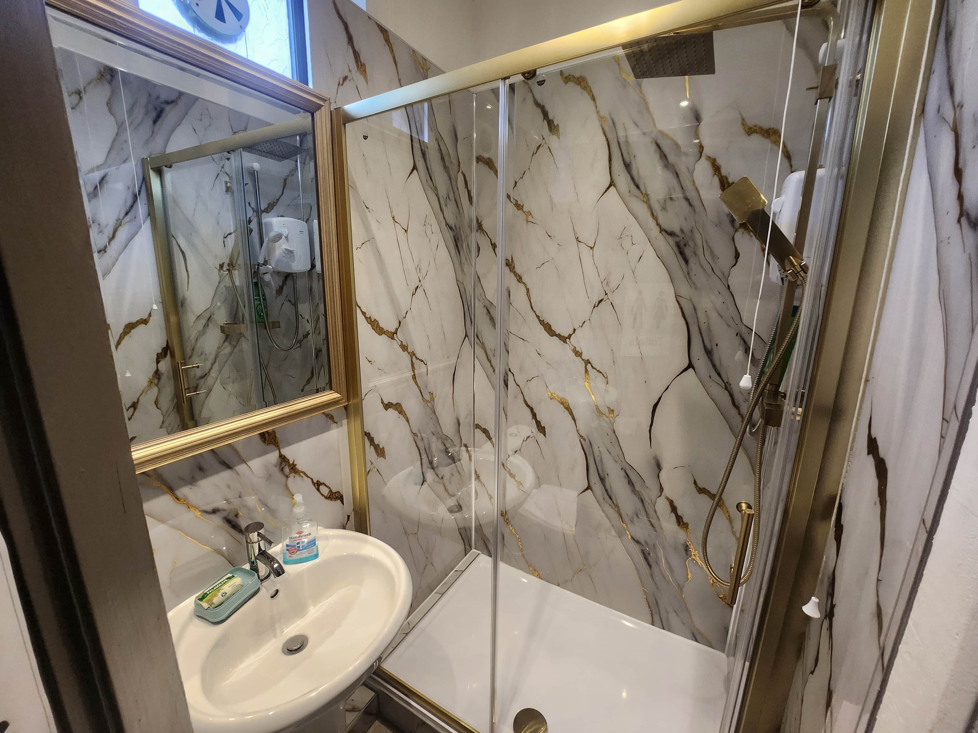 Une salle de bain dotée d’un meuble-lavabo en marbre, d’une douche à parois de verre et d’un miroir avec un cadre doré.
