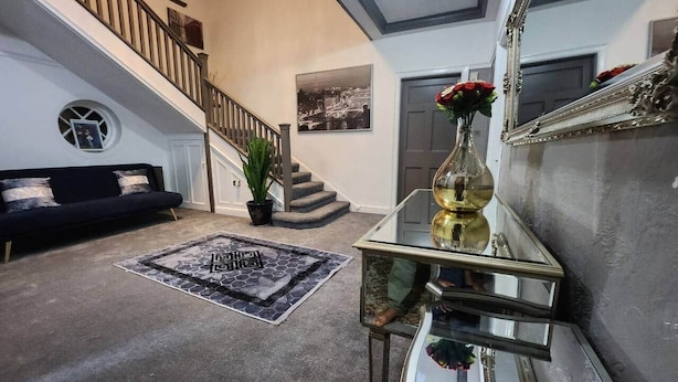 A spacious living area with a staircase, a black sofa, a patterned rug, and a glass coffee table with a vase of flowers. - Room 1 Cottage   White House Old Trafford  Manchester (Stretford)