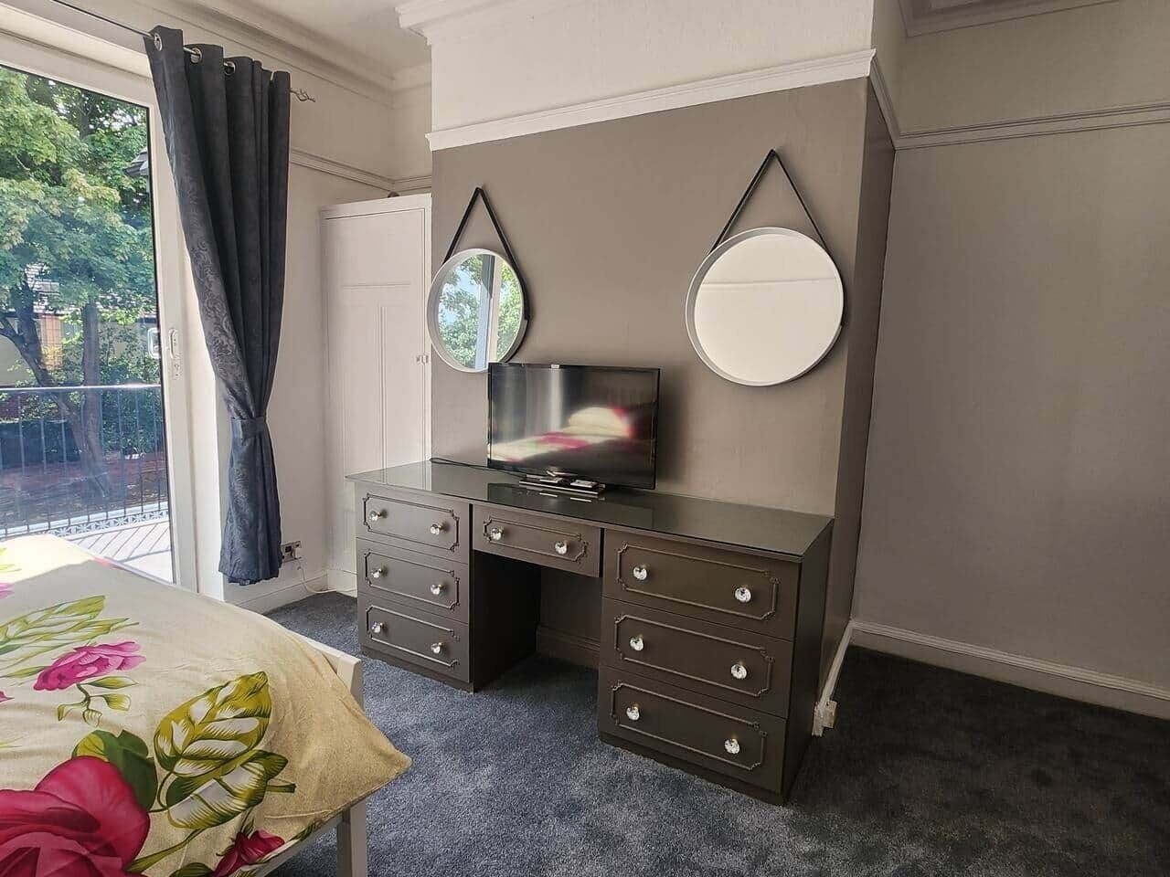 A bedroom with a bed, a dresser, two wall mirrors, and a TV.