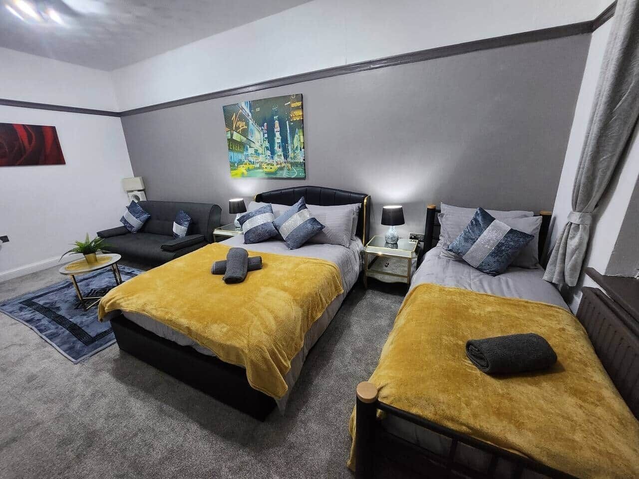 A hotel room with two beds, a nightstand, a lamp, a small table with a plant, and a painting on the wall.
