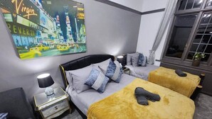 Ein Hotelzimmer mit einem Bett, zwei Nachttischen, einer Lampe, einem Fenster und einem Stadtbild an der Wand.