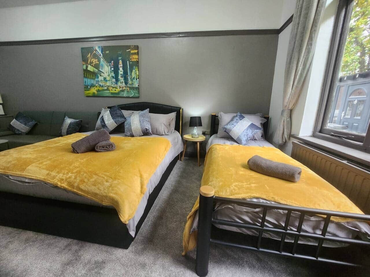 A hotel room with two beds, a painting on the wall, a small table, and a window with curtains.