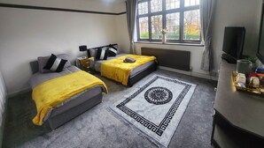 Ein Zimmer mit zwei Betten, einem großen Fenster, einer Heizung, einem Fernseher und einem dekorativen Teppich.