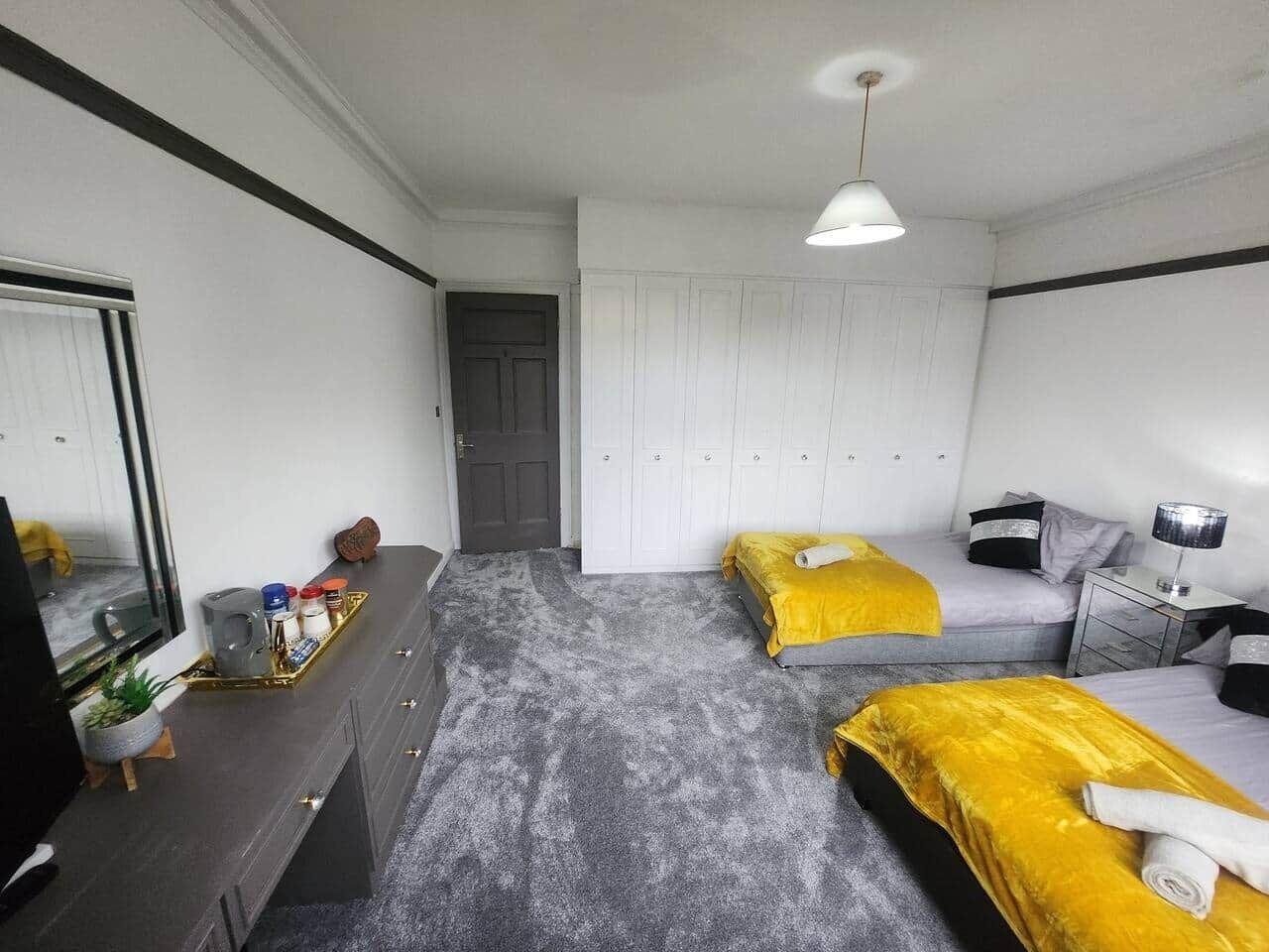 A hotel room with two beds, a desk, a mirror, and a wardrobe.