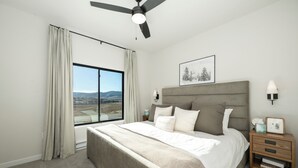 Quarto com cama grande, ventoinha no teto, mesa de cabeceira com luminária e janela com cortinas.