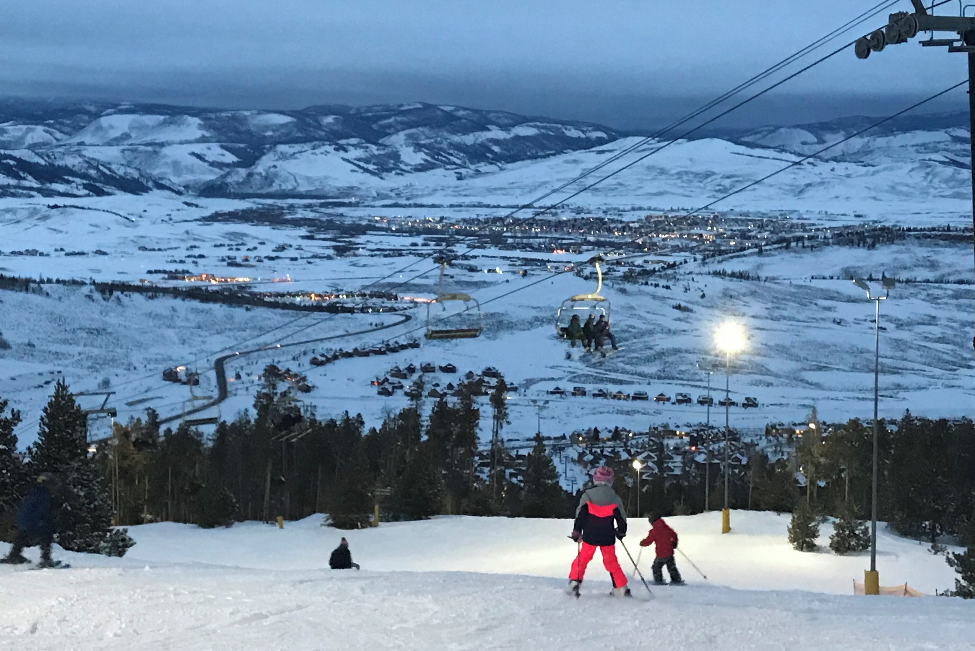 En snötäckt skidbacke med en skidlift och en stad i bakgrunden.