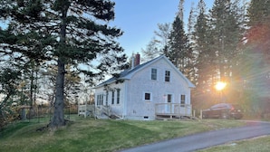 A white two-story house with a front porch, a driveway, and a parked car.
