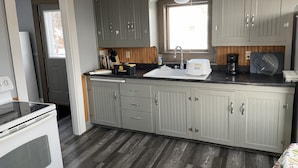 A kitchen with grey cabinets, a white stove, and a window above the sink.