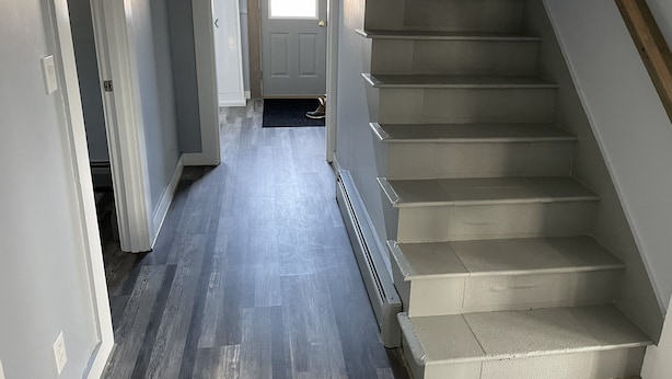 A hallway with a wooden floor leading to a staircase with beige steps and a wooden handrail.