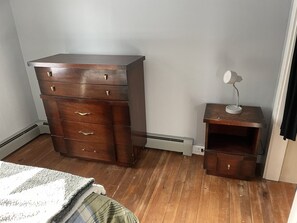 Une chambre à coucher avec une commode en bois, une table de chevet avec une lampe et un lit recouvert d’une couverture verte.