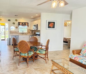 A spacious living area with a dining table and chairs, a kitchen with white cabinets and a microwave, and a wicker sofa with a colorful cushion. - 3752 San Carlos Drive (Dockside Dreams): 3 BR, 2 BA House in Saint James City, Sleeps 7 (Saint James City)