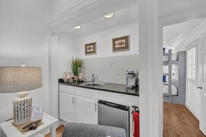 Una cocina moderna con armarios blancos, encimera negra y lavavajillas integrado. Hay dos cuadros en la pared, una planta en maceta y una lámpara en la encimera.