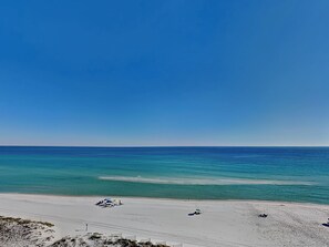 A beach with clear blue water, sandy shore, and a few umbrellas.