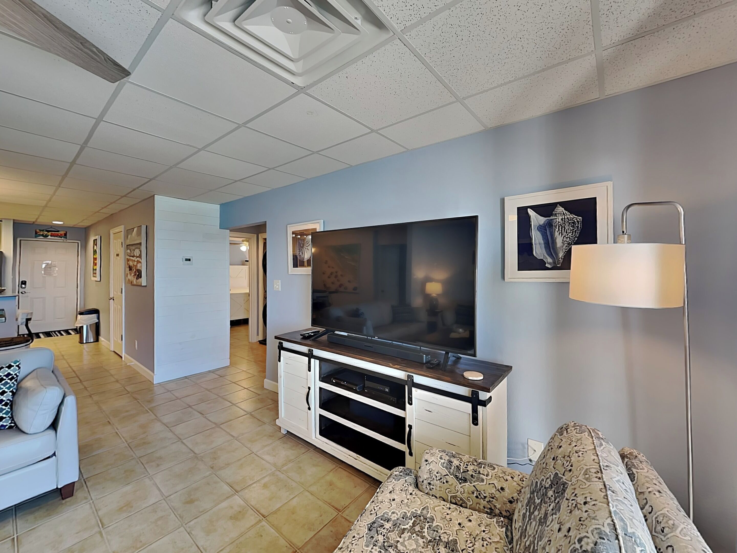 A living room with a flat-screen TV, a sofa, a coffee table, and a lamp.