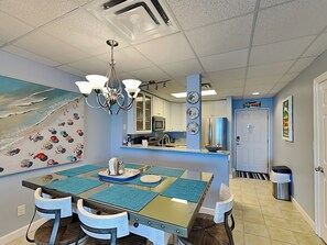A dining area with a glass table, blue placemats, and a chandelier.