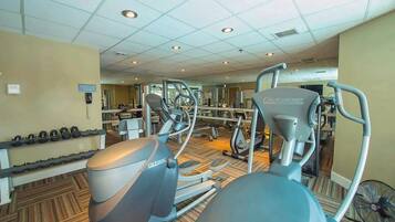 Une salle de sport équipée de tapis de course, de vélos elliptiques et d’un mur recouvert de miroirs.