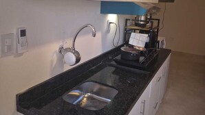 A kitchen with a granite countertop, stainless steel sink, white cabinets, and a built-in microwave. - Edificio Navarra (Asunción)