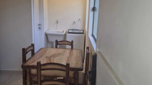 A compact dining area with a wooden table and chairs, a small sink, and a window. - Edificio Navarra (Asunción)