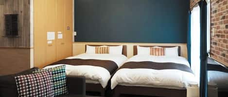 A hotel room with two beds, a sofa, a ceiling fan, and a brick wall.