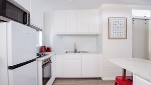 Een moderne keuken met witte kastjes, een roestvrijstalen koelkast, een magnetron, een rode broodrooster en een spoelbak.