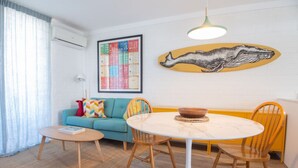 Een gezellige woonkamer met een ronde tafel, twee stoelen, een bank en een kleurrijk kunstwerk aan de muur.