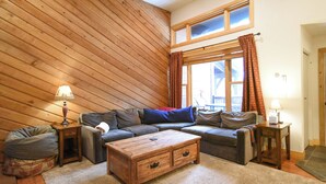 Een gezellige woonkamer met een houten schuine daklijn, een hoekbank, een houten salontafel en een poef.